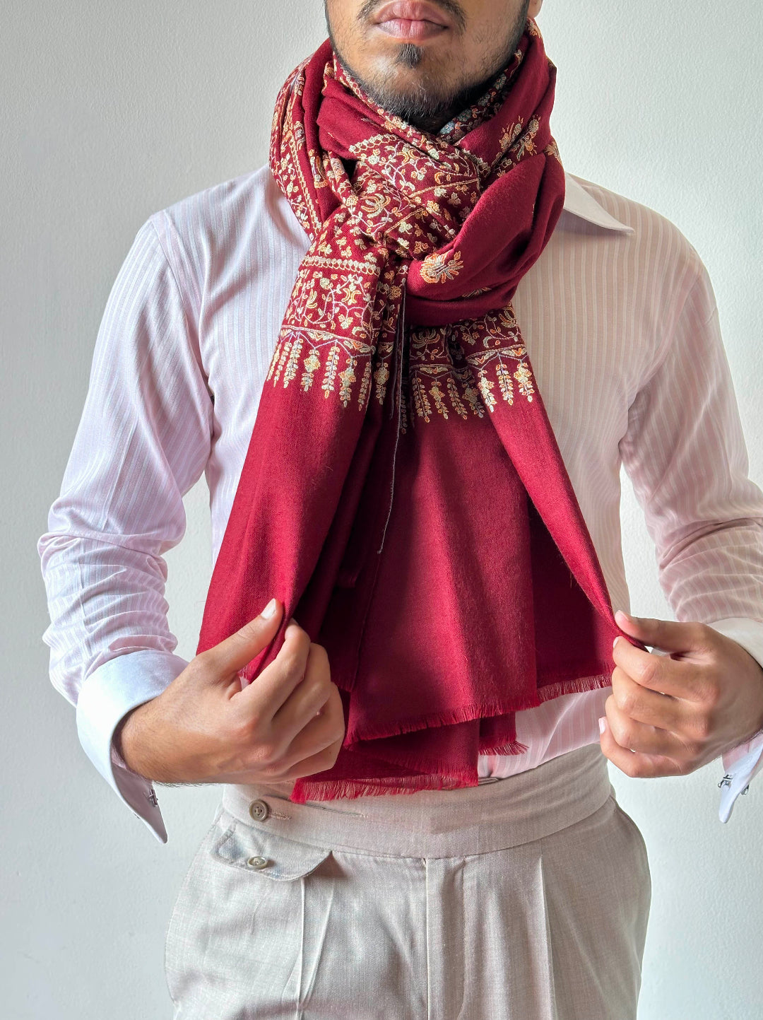 Man wearing a red patterned scarf over a white shirt and pants on a plain background