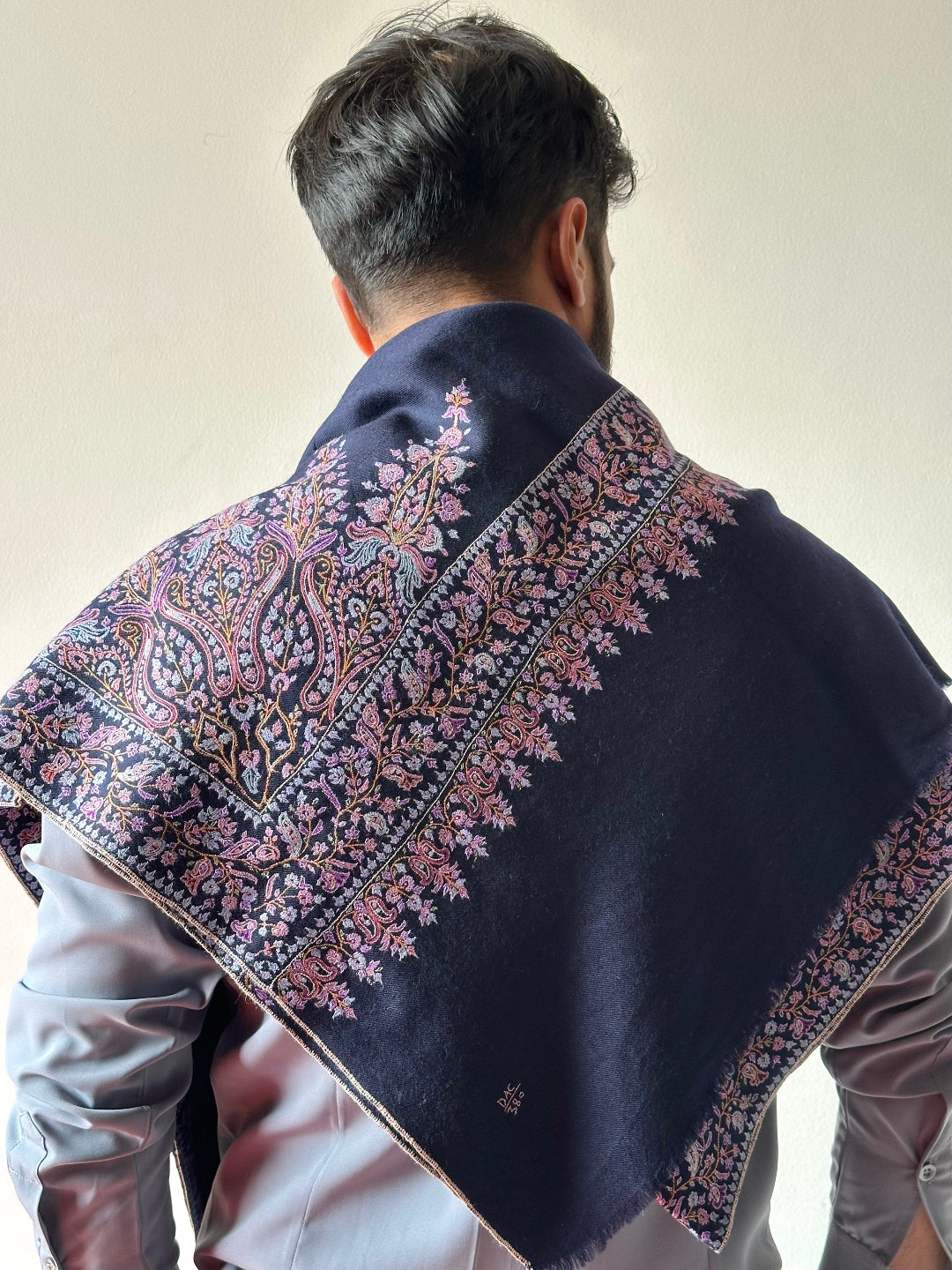 Person wearing a dark blue shawl with intricate floral patterns on a plain background